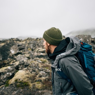 Dans un temps hivernal, un randonneur coiffé d'un bonnet admire un paysage minéral. 