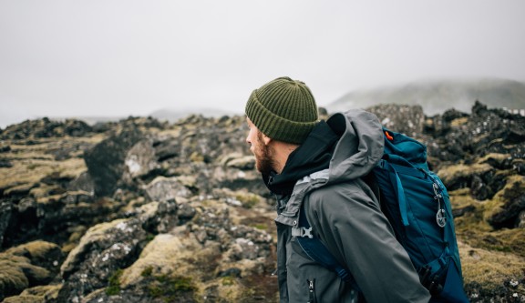 Dans un temps hivernal, un randonneur coiffé d'un bonnet admire un paysage minéral. 